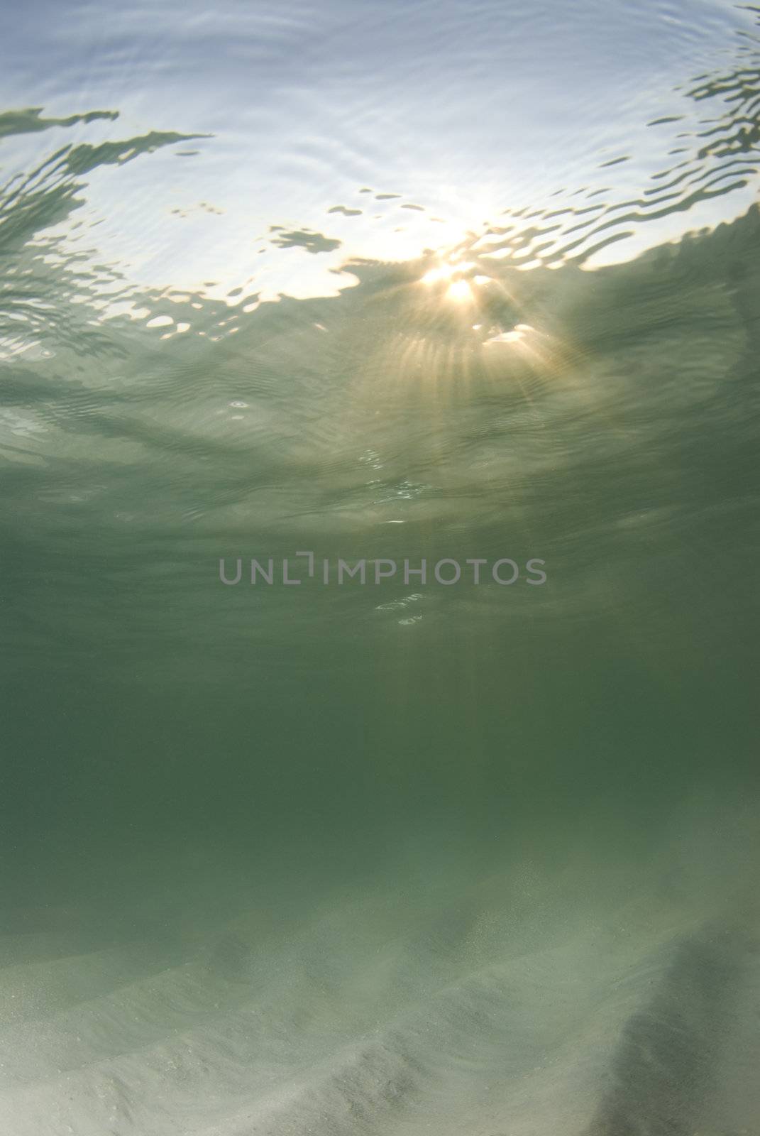 A view of the rippled ocean floor, the action on the surface, and the sky and golden sunset rays breaking through the water.  Sunrays in top third.