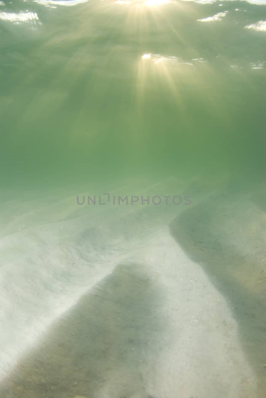 A view of the rippled ocean floor, the action on the surface, and the sky and golden sunset rays breaking through the water. Double top sunrays.
