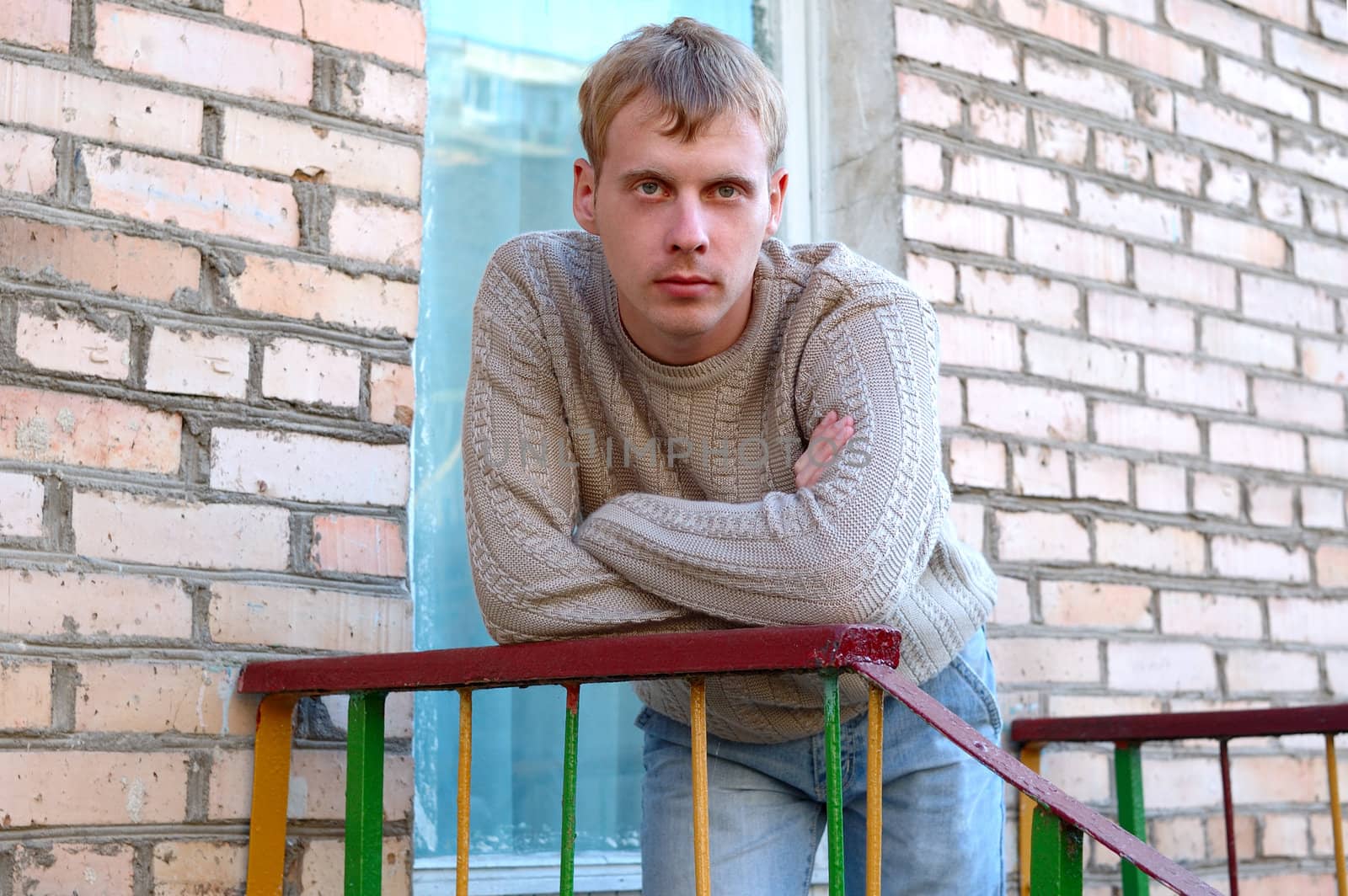 Young stylish man with blonde hair stay on stairs near brick wall.