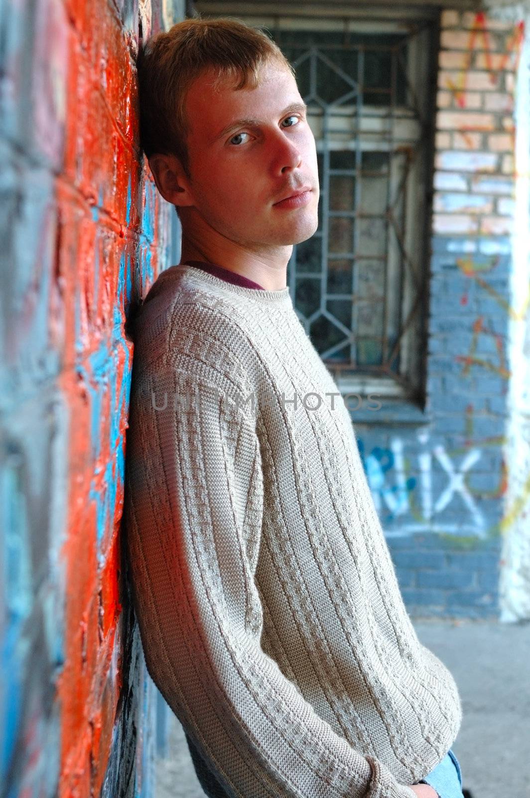 Young stylish man with blonde hair stand near graffiti brick wall.