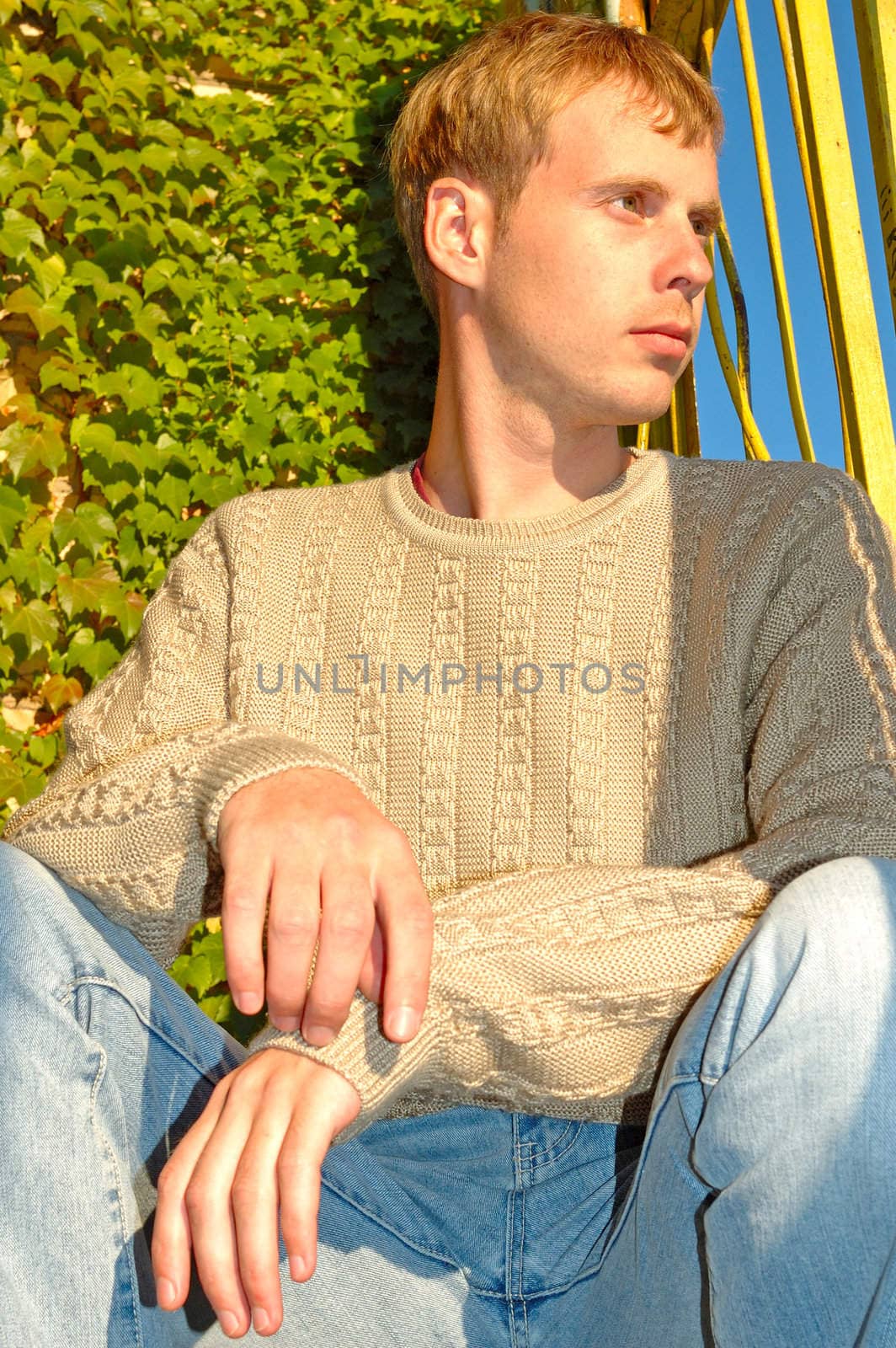 Young stylish blonde man sit near overgrown with vine wall.