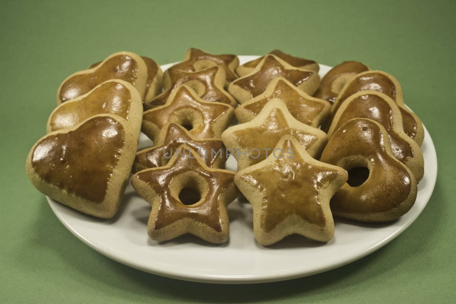 Star and heart gingerbread cookies on white plate isolated on green paper