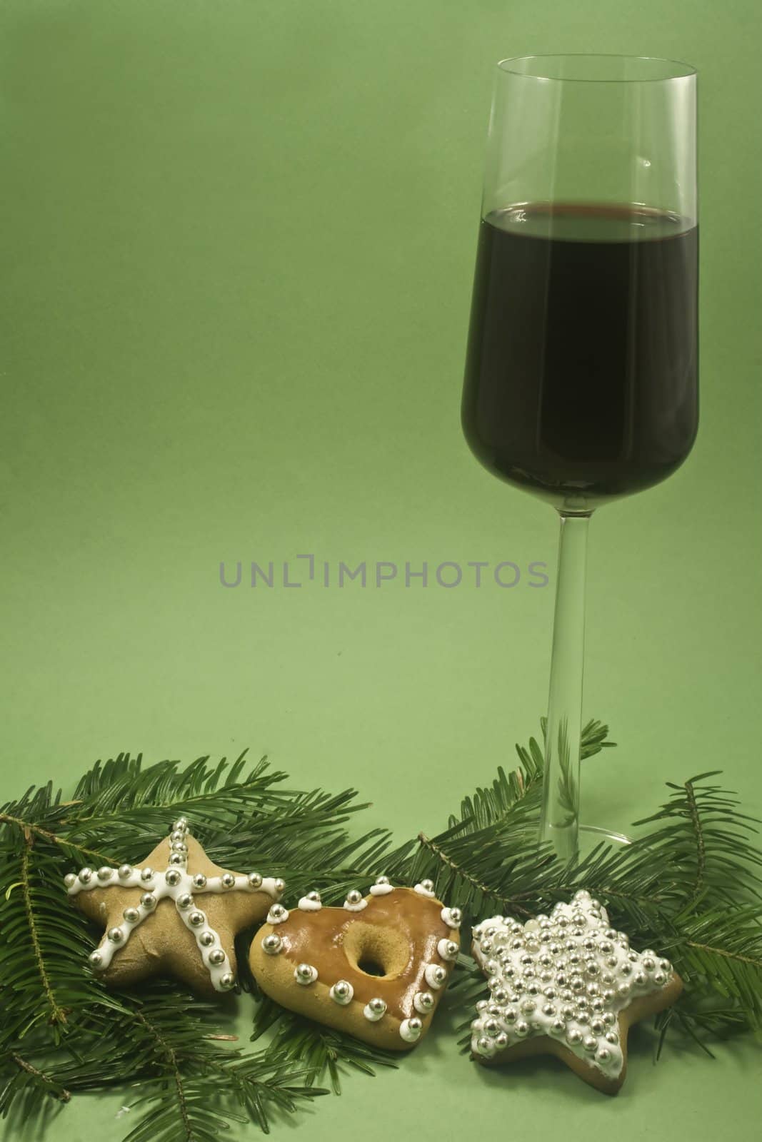 A glass of red wine and three decorated cookies with fir branch isolated on green paper