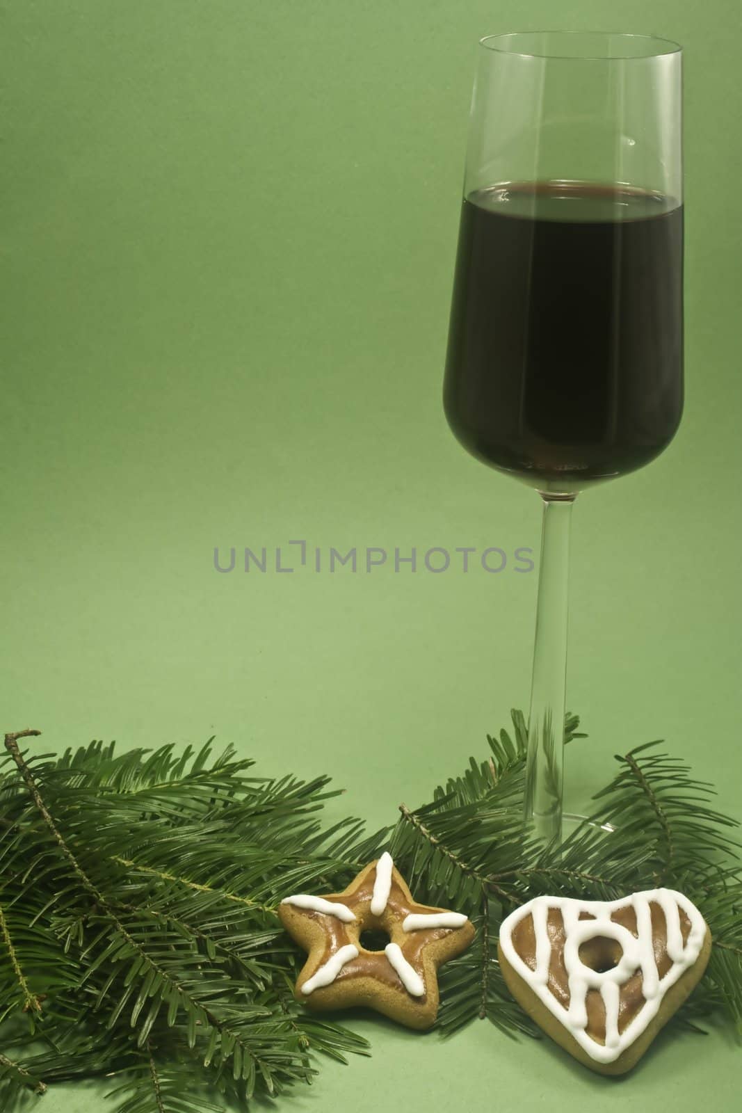 A glass of red wine and two cookies on a fir branch isolated on green paper