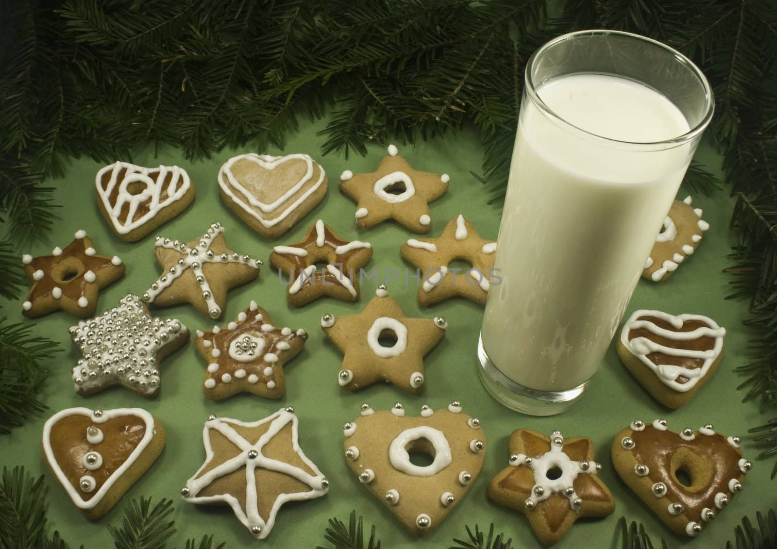 A variety of decorated Christmas cookies with a glass of milk surrounded by fir branches