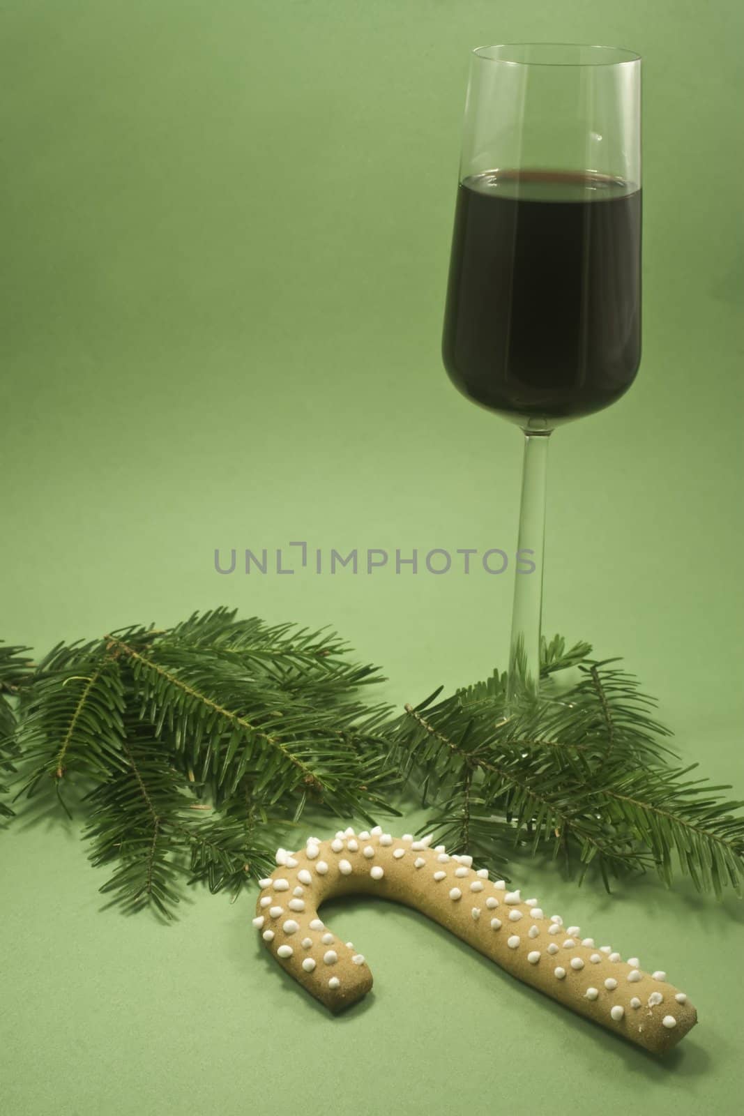 A glass of red wine and candy cane cookie with fir branch isolated on green paper