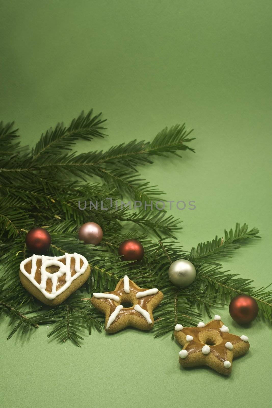 Three cookies and five shiny balls on fir branch isolated on green paper