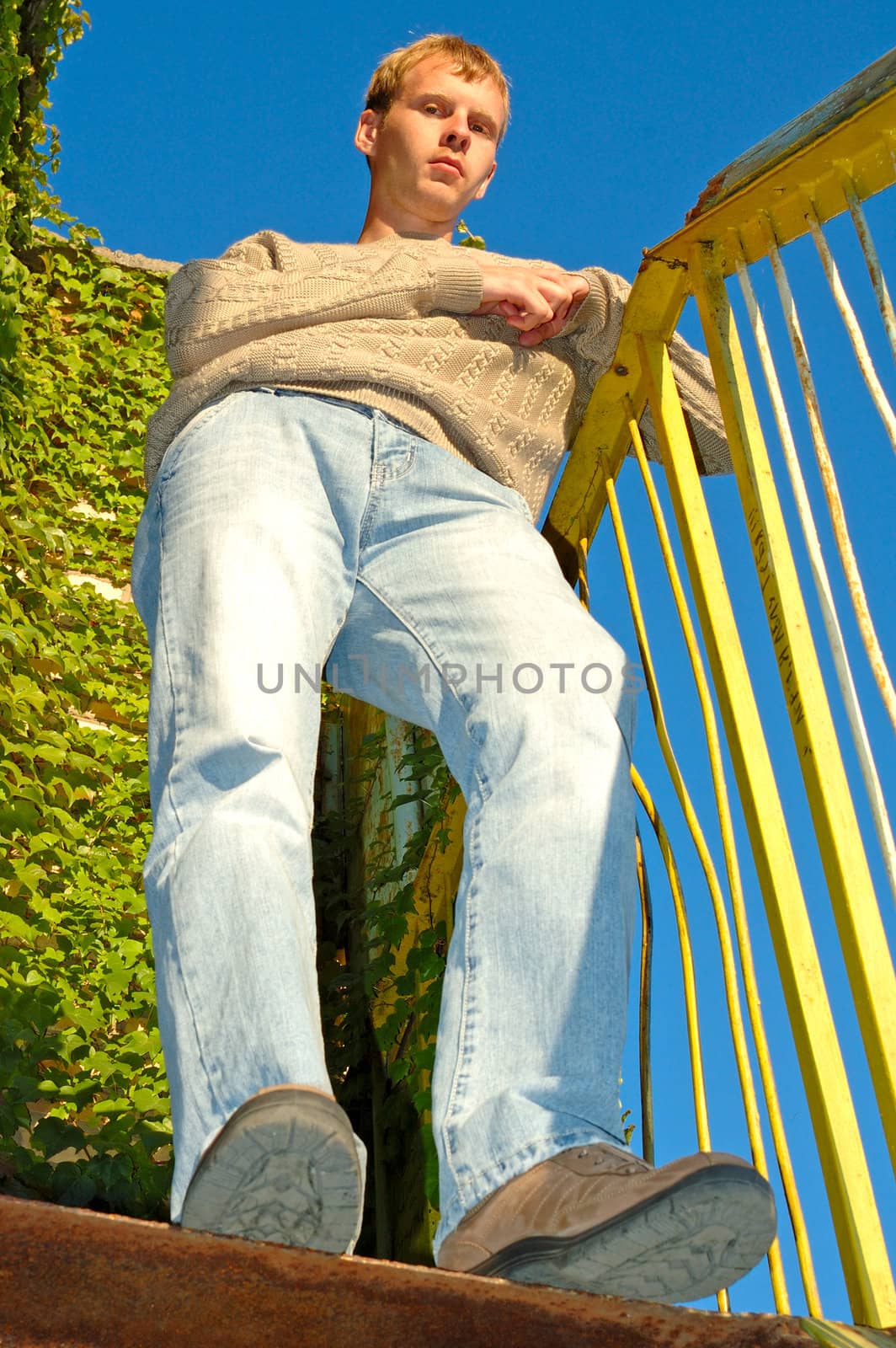 Young stylish blonde man stay on stairs near overgrown with vine wall.