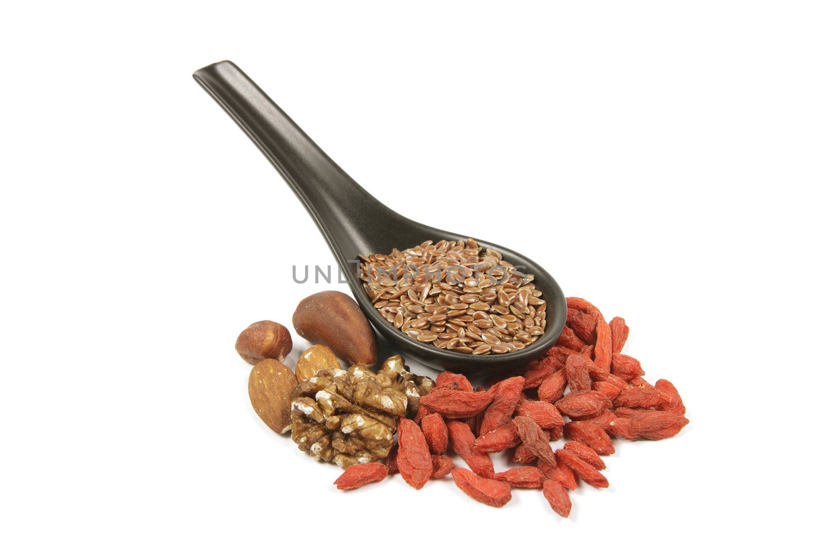 Brown linseed seeds on a small black spoon with mixed nuts and goji berries on a reflective white background