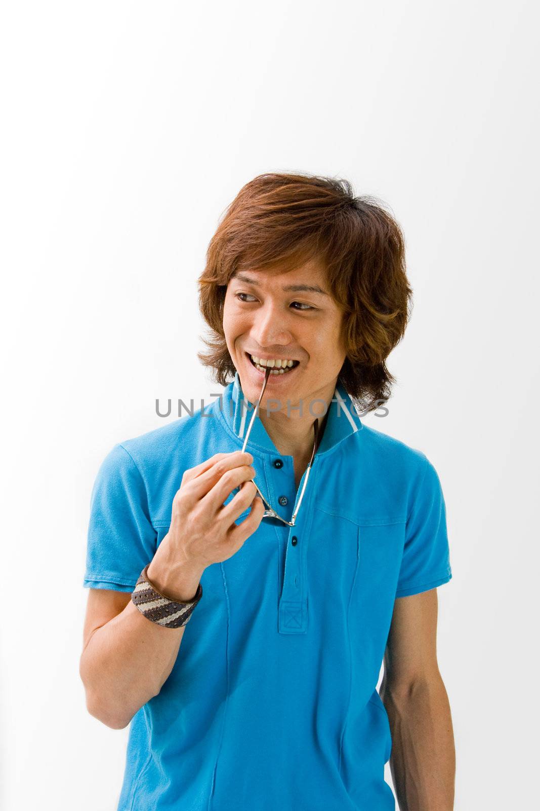 Smiling Asian guy in blue t-shirt holding sunglasses and biting on it, isolated