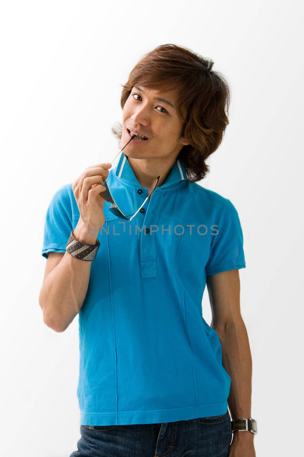 Happy Asian guy in blue t-shirt holding sunglasses and biting on it, isolated