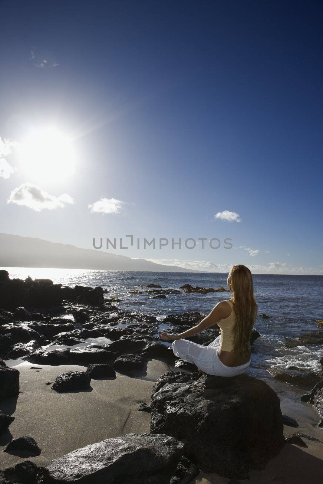 Young adult Asian Filipino female meditating on rocky beach in Maui Hawaii.