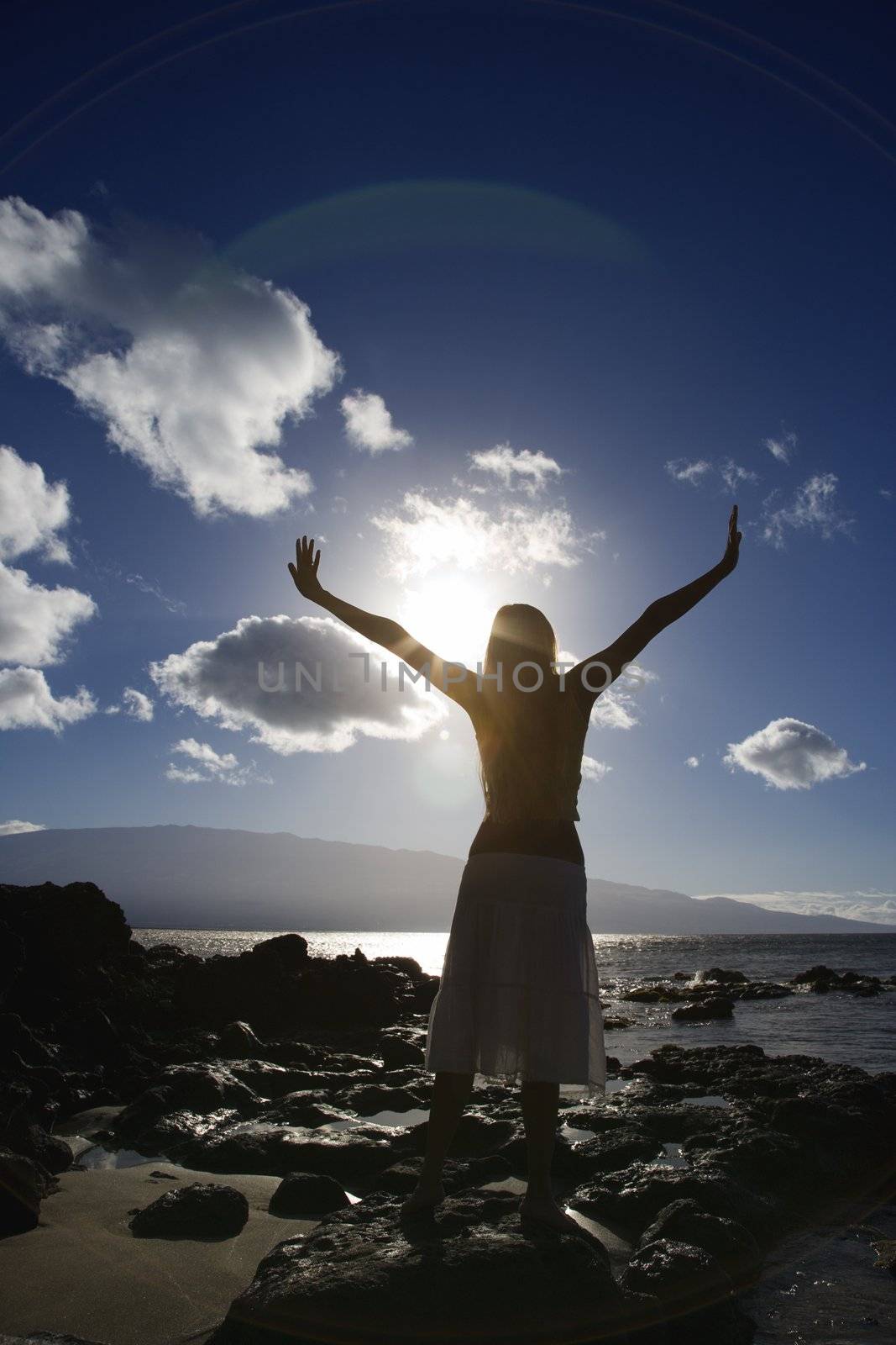 Young adult Asian Filipino female stretching arms in air on beach in Maui Hawaii.