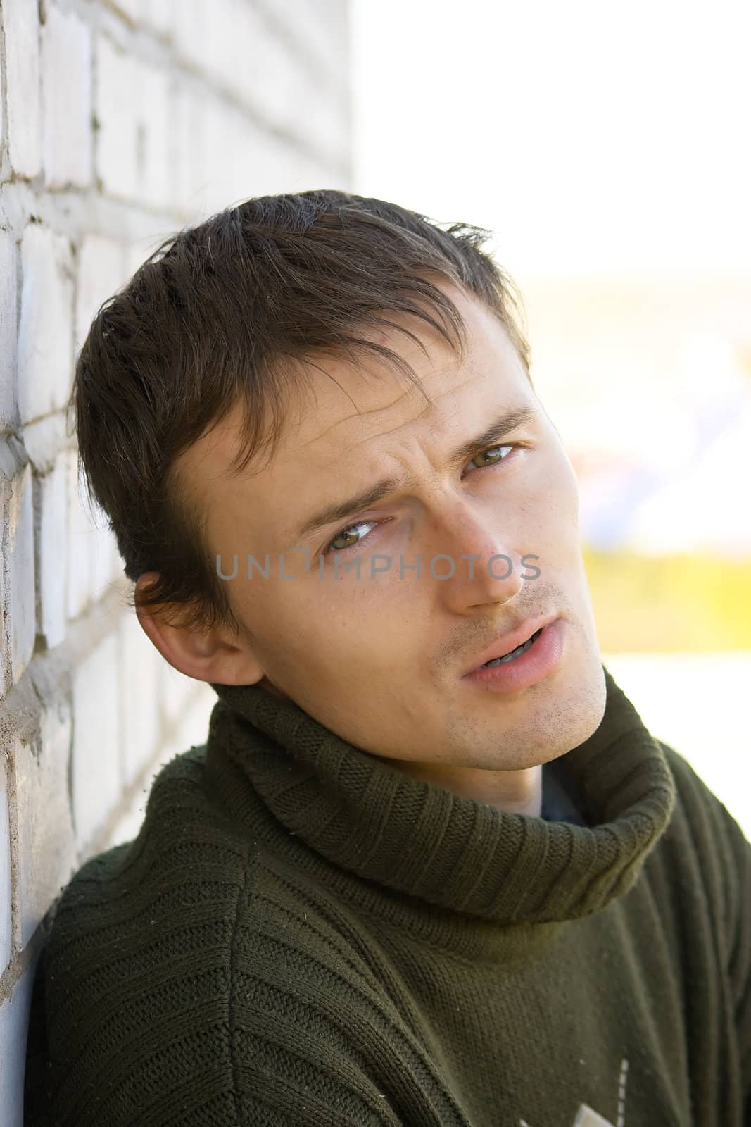 Portrait of the sad young man in a green sweater on an abstract background