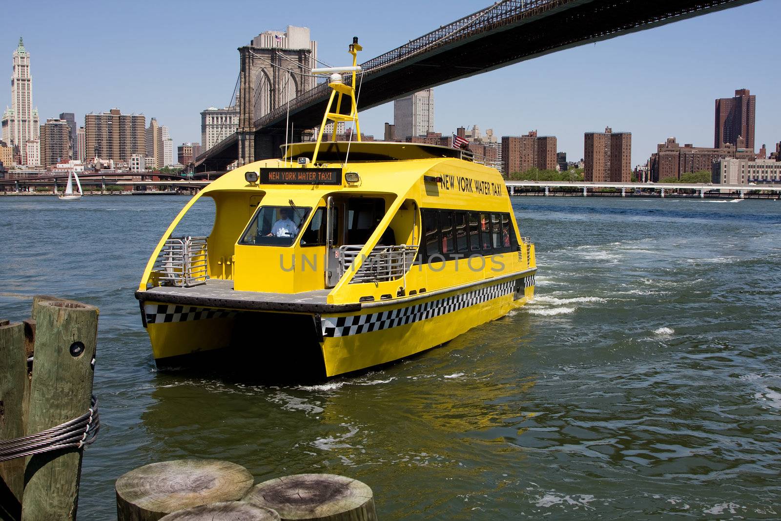New York City's water taxi arriving at Fulton Ferry landing in Brooklyn. Here seen with the Brooklyn Bridge in the background on a bright sunny day with a depp blue sky.