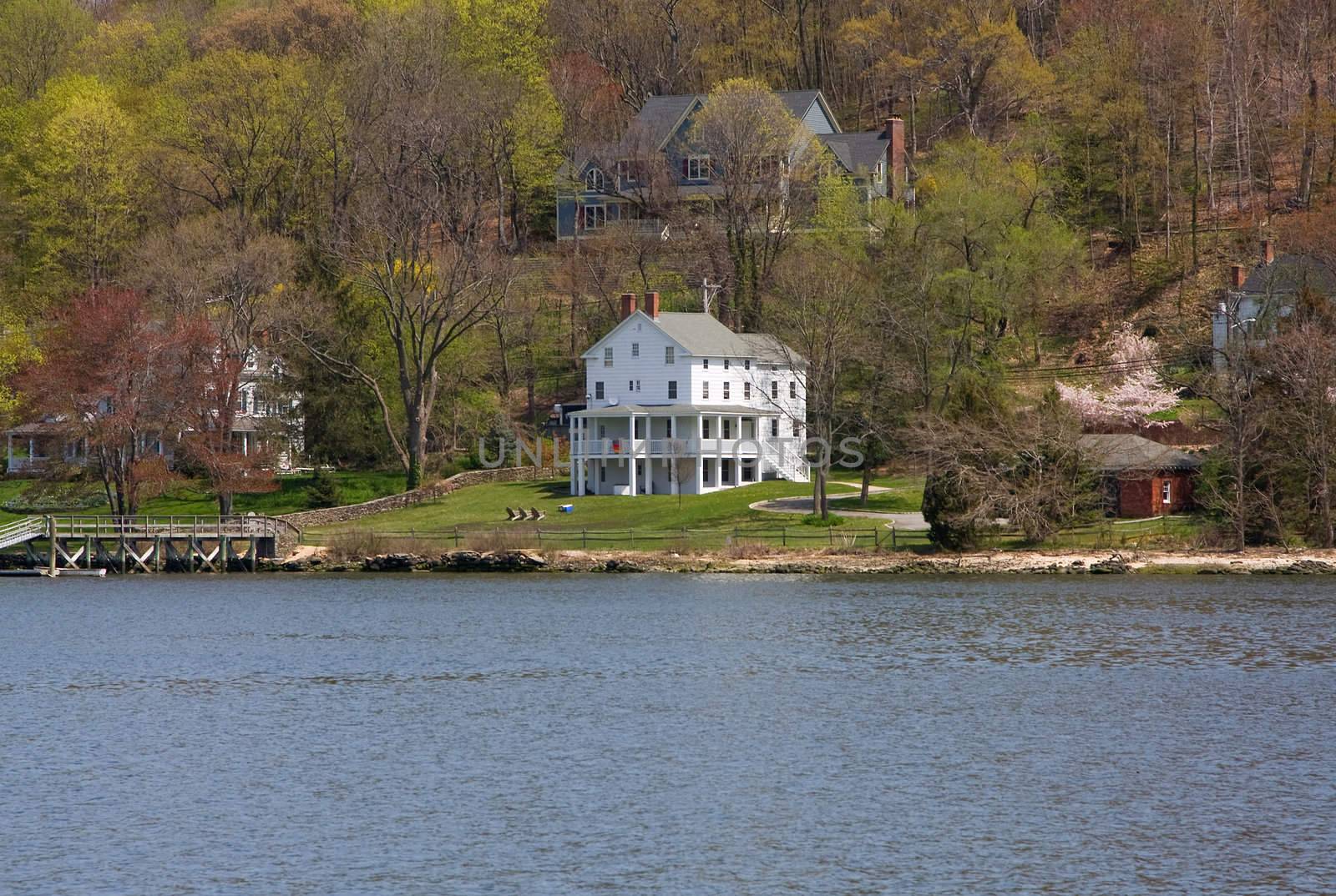 A remotely located white Victorian mansion on the water and in the woods on a spring day.