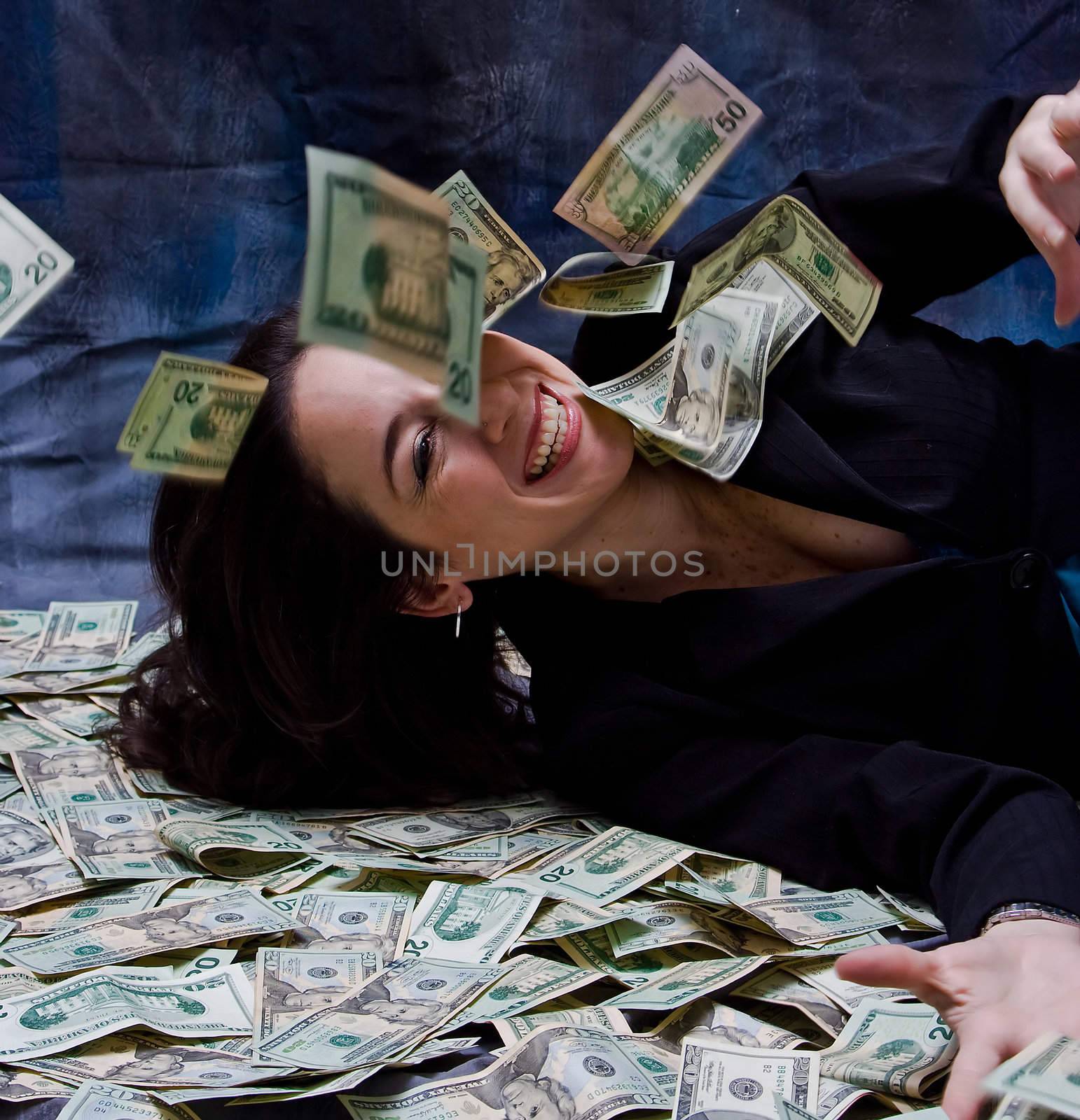 Rich business woman waving laying with her money, she smiles as money falls out of the sky, isolated on a dark background