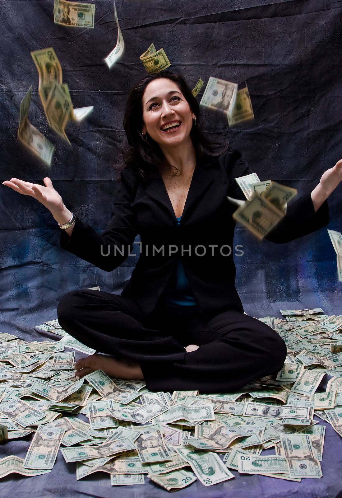 Rich woman sitting with open arms in money and as money falls out of the sky isolated on a dark background