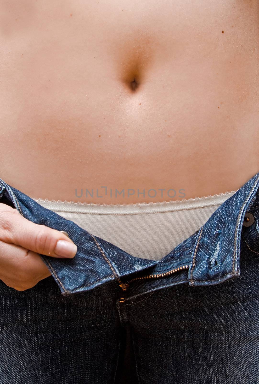 Young woman opening her blue jeans showing a rim of her white underware and bare belly up to her bellybutton