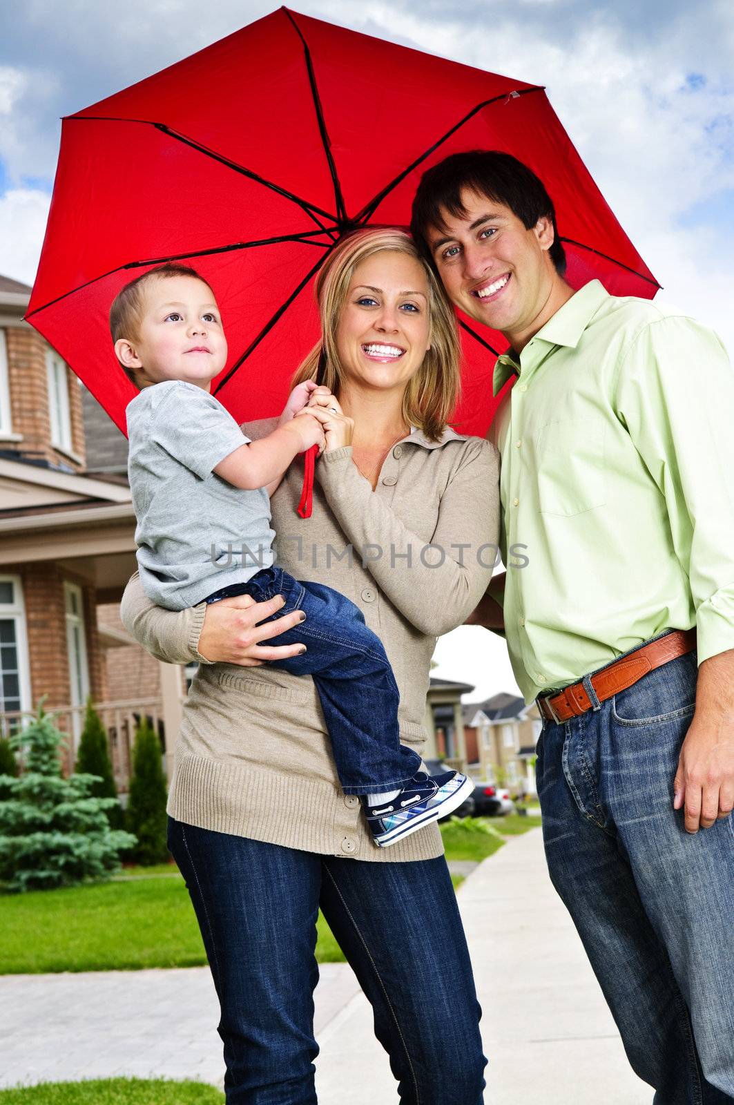 Young happy family under umbrella on sidewalk