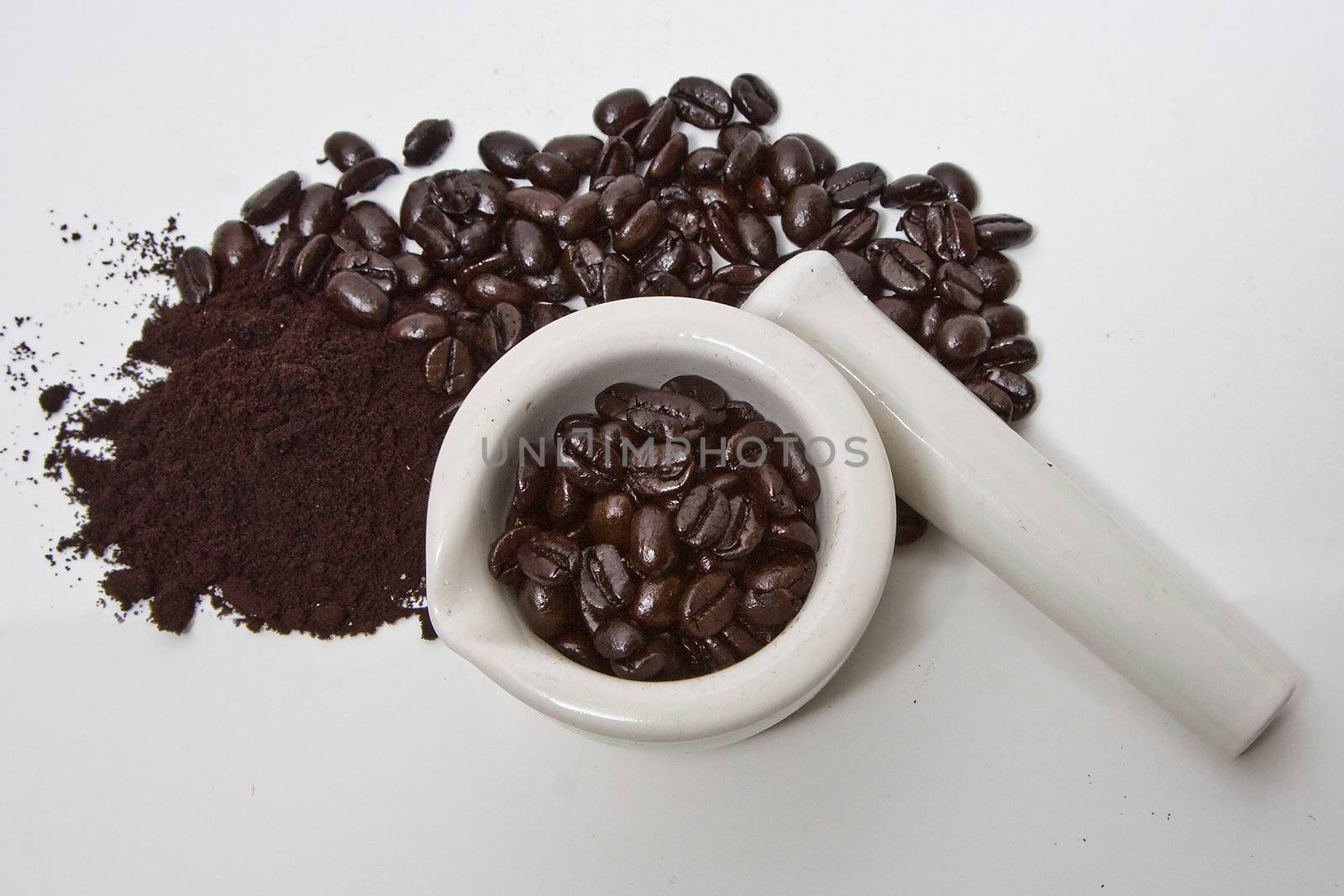 A mortar filled with freshly roasted gourmet coffee beans, with coffee beans and grind next to it isolated on a white background