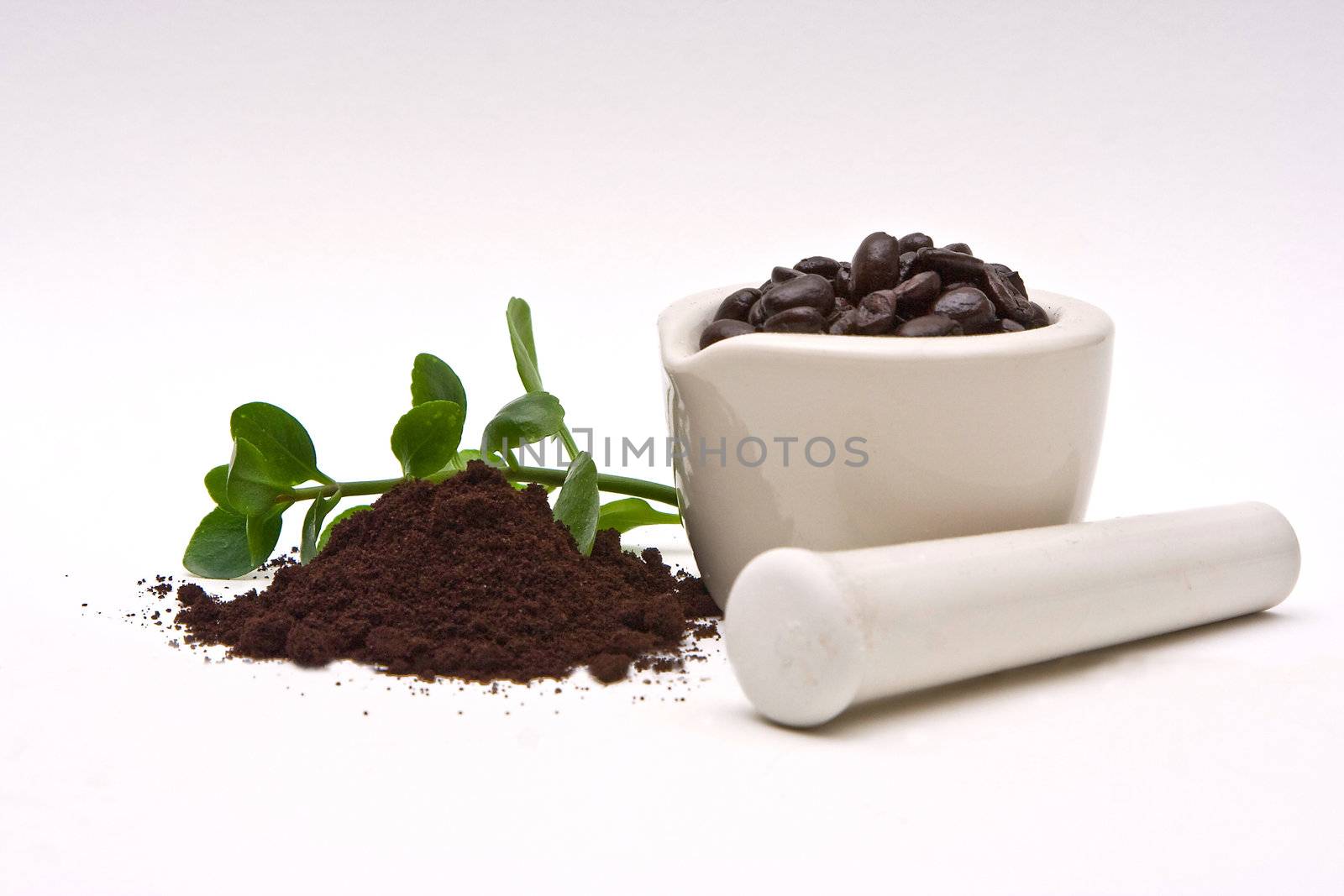 A mortar with freshly roasted coffee beans and a pile of coffee grind with some leaves in the back on a white background