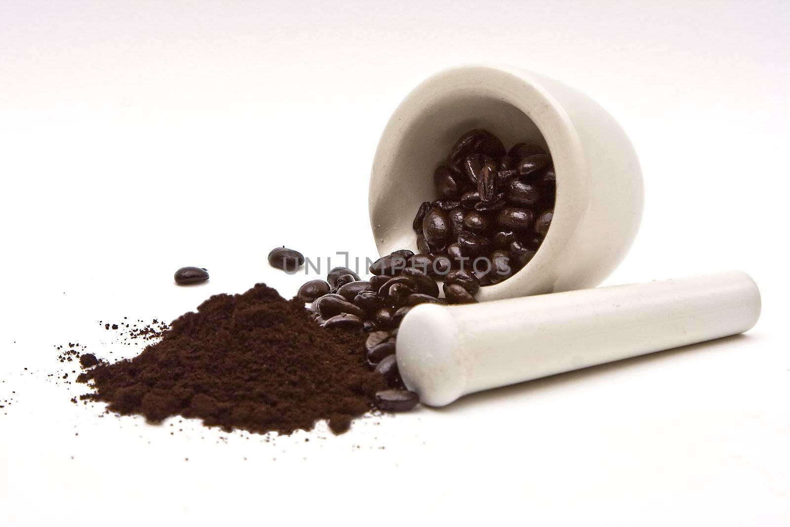 A mortar with freshly roasted coffee beans spilled out with in front a pile of coffee grind; on a white background