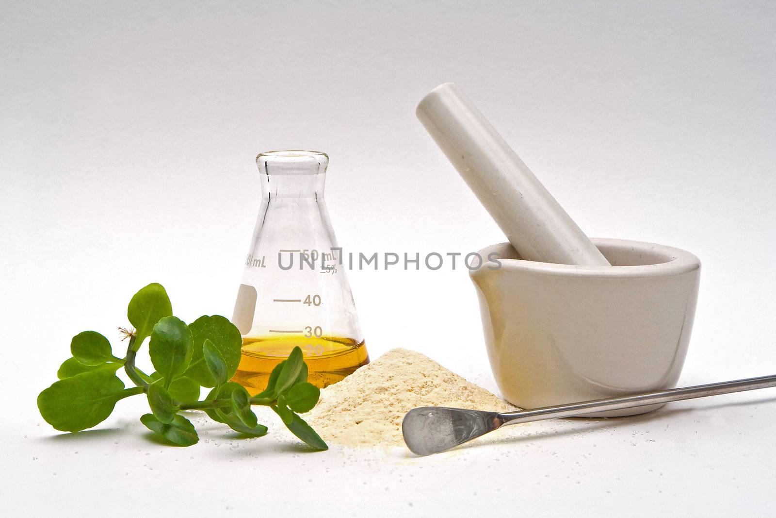 A yellow liquid in a flask with a powder and some leaves in front with a white mortar and a silver spatula on a white background