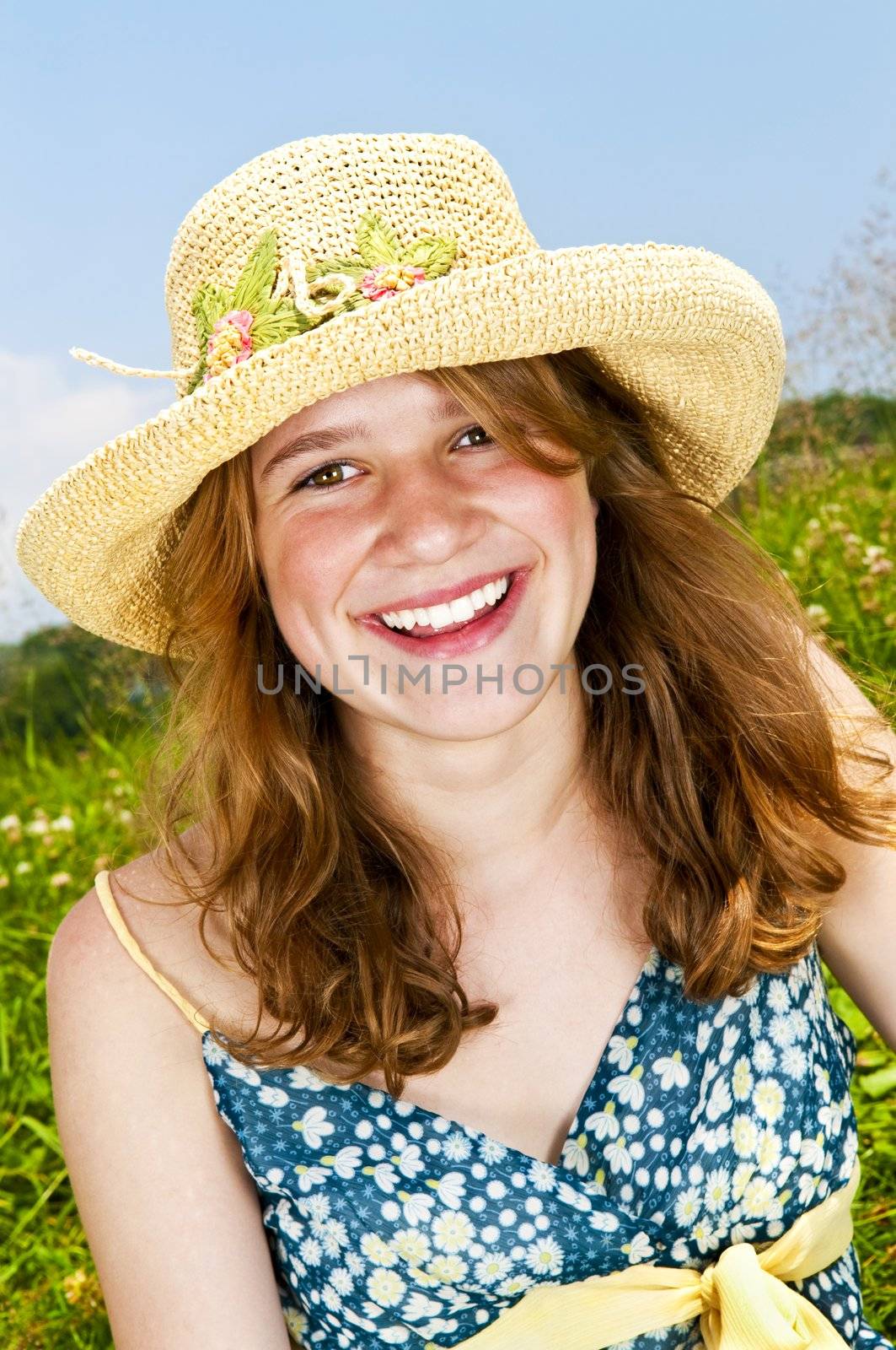 Portrait of young teenage girl smiling on summer meadow in straw hat