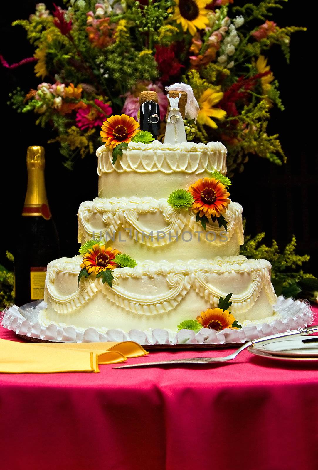 A white wedding cake accompanied with a variety of flowers. The cake is sitting on a table with a fuchsia table cloth.