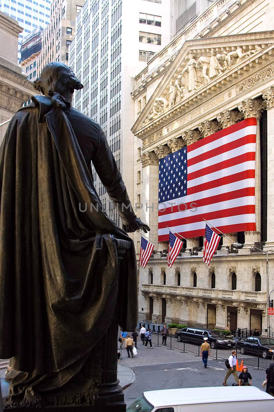 A statue of former President George Washington pointing towards the American Flag hanging on the New York Stock Exchange building on Wall Street