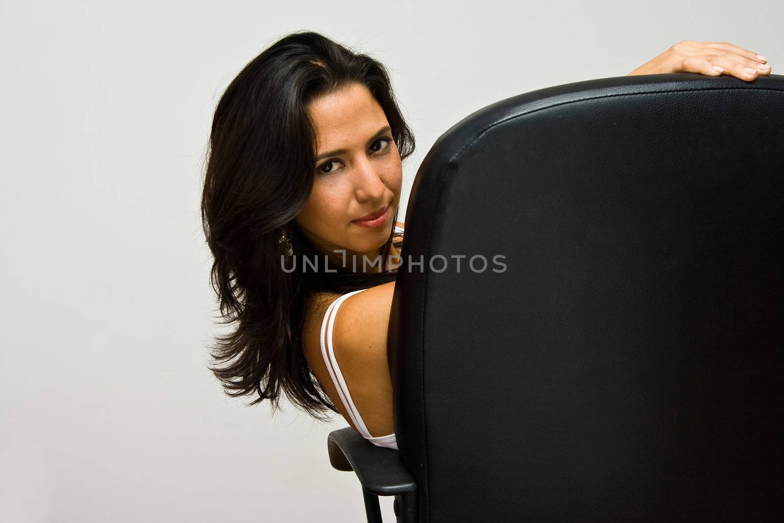 A beautiful young latina woman sitting in a desk chair and looking back, isolated on white
