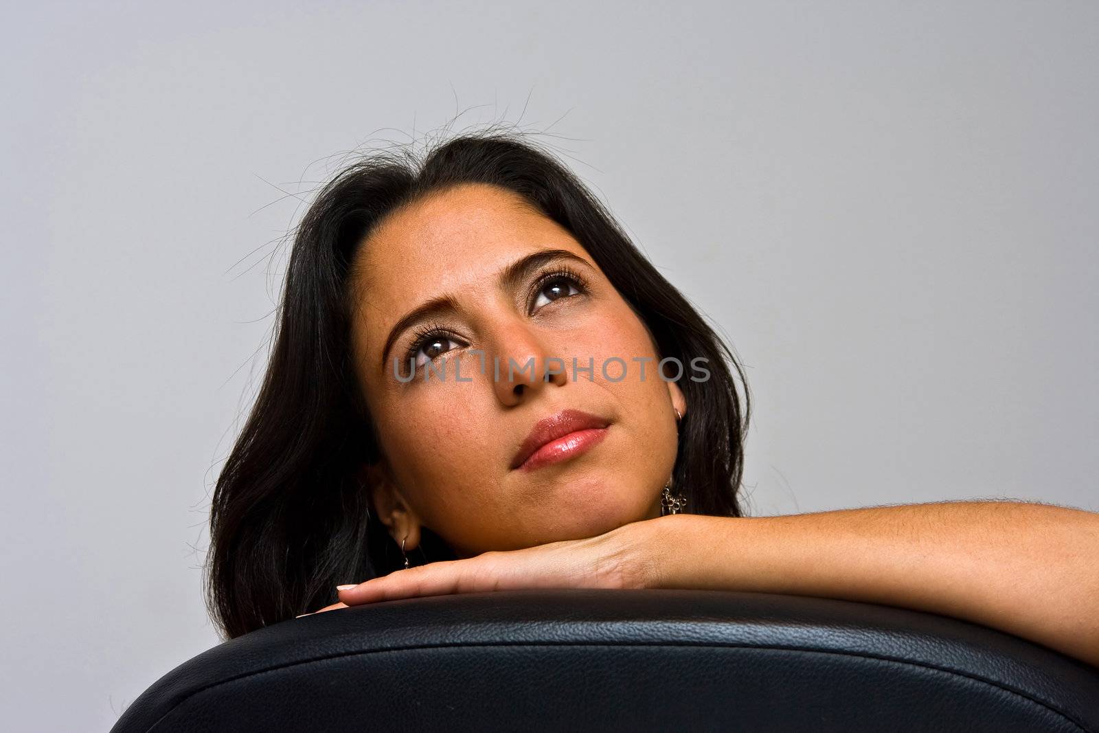 A beautiful young hispanic girl day dreaming, looking up with her shiny eyes and supporting her head with her hand, isolated on white