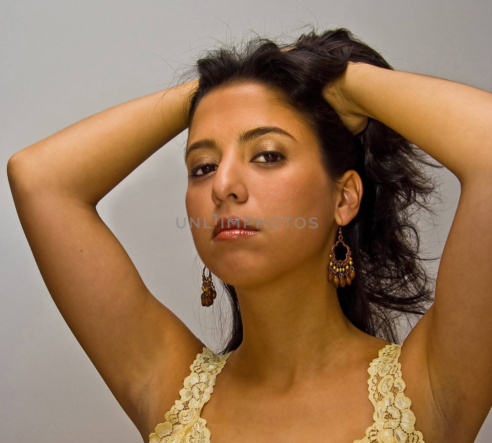 Beautiful dark brown haired latina woman with both her hands in her hair, wearing a yellow shirt, deep red glossy lips and gold eyeshadow, isolated on white