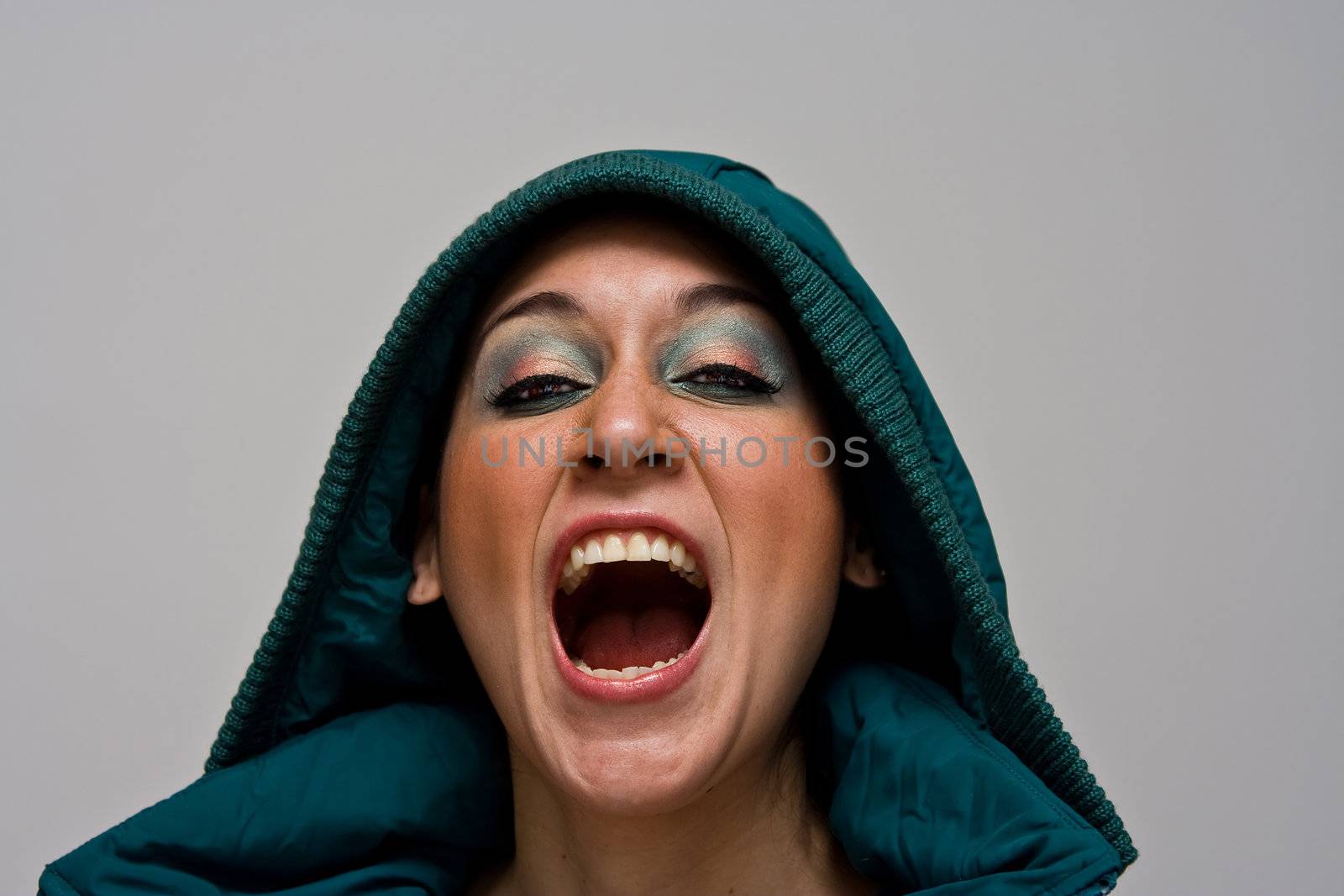 A beautiful young woman screaming aggressively wearing a green winter coat and the hood over her head, isolated on white