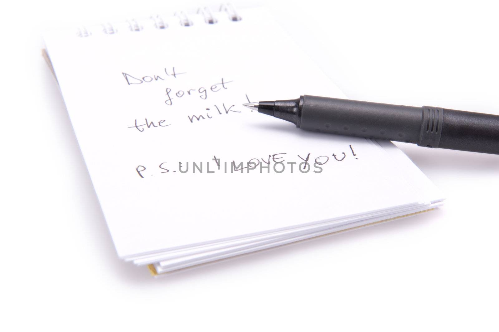 Closeup of a notebook with a shopping reminder on it and a black pen. Isolated on white.