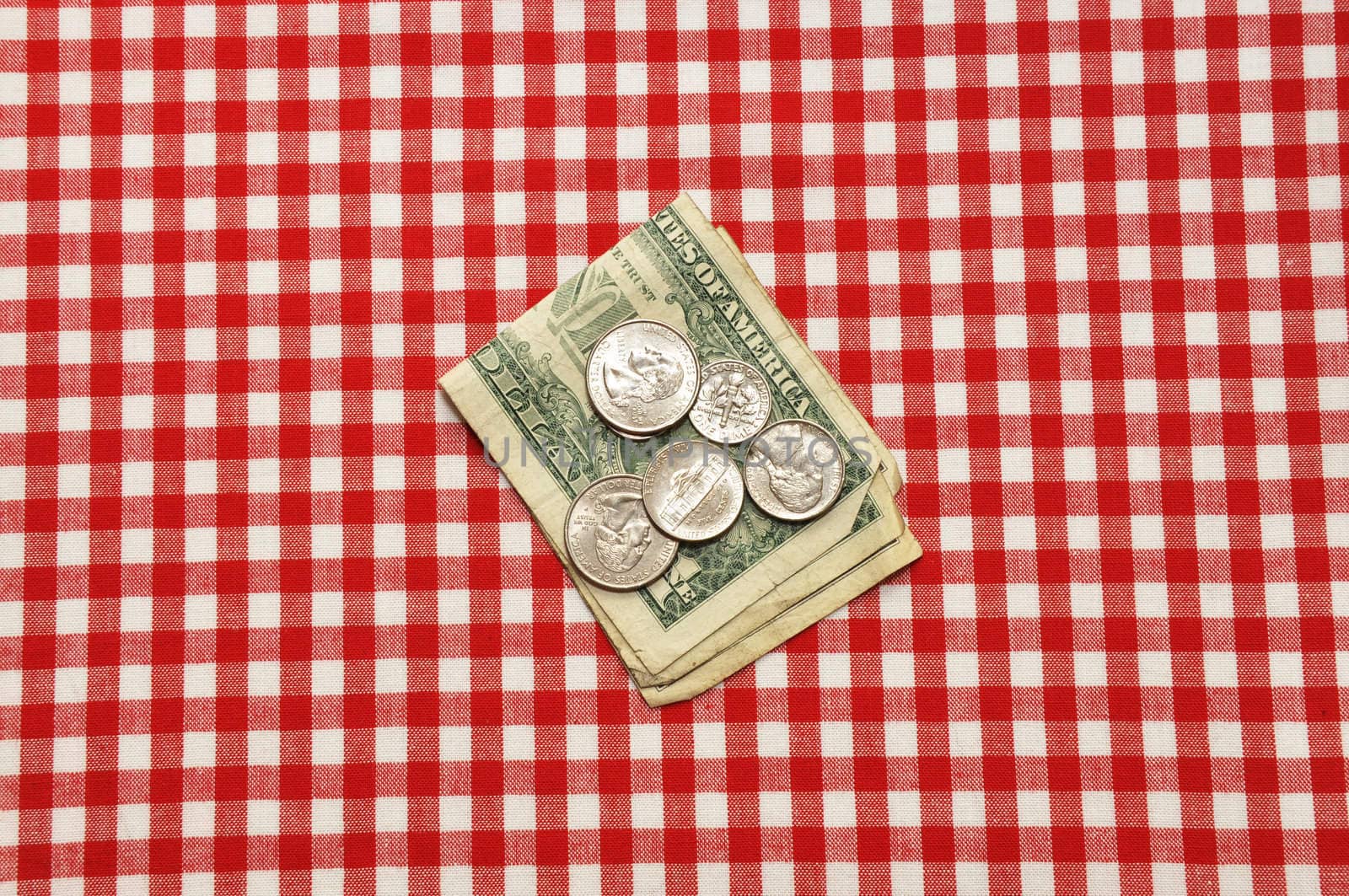 Tip left on restaurant table.  Bills and coins on red gingham tablecloth.  
