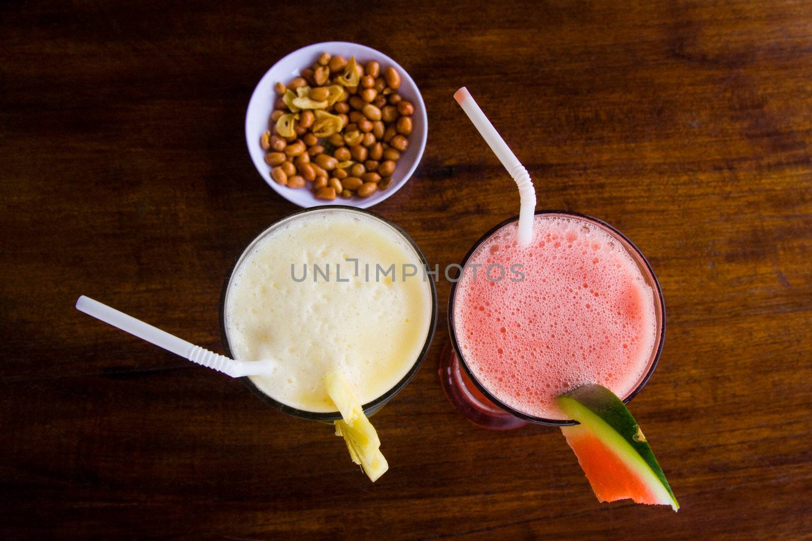 Two cocktails with drinking straw and peanuts on table.