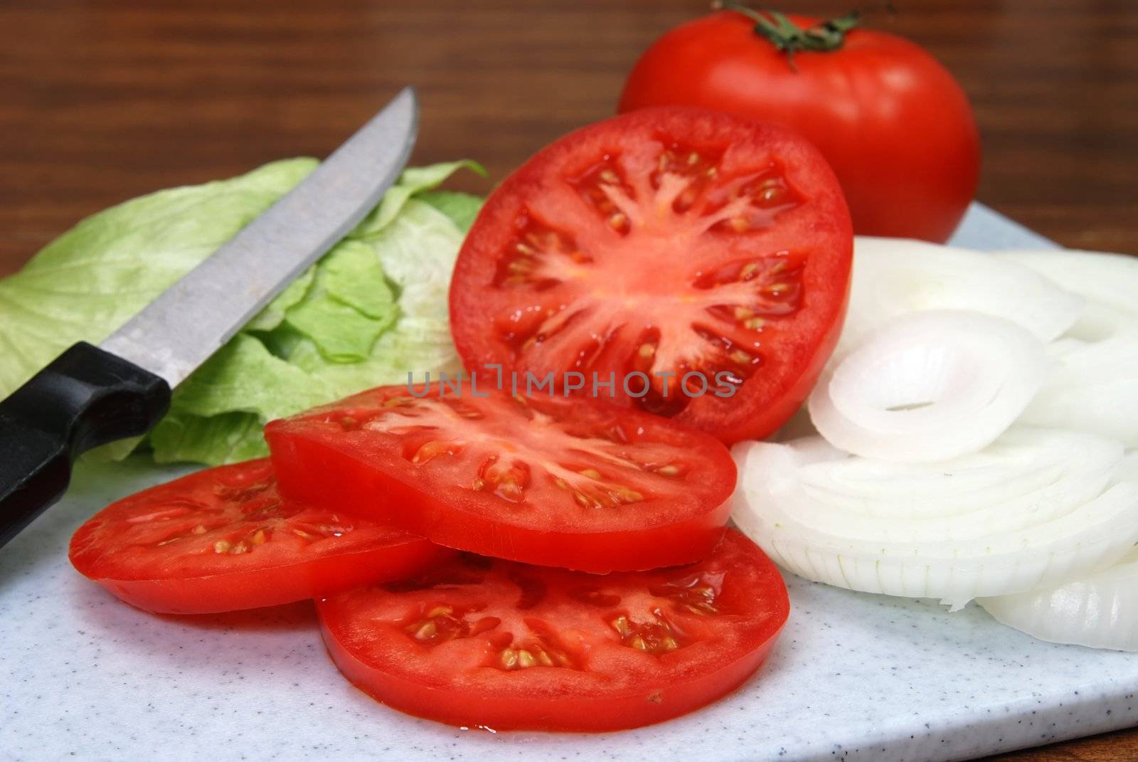 Tomato, lettuce, onions, and knife on cutting board.  Shallow depth of field.