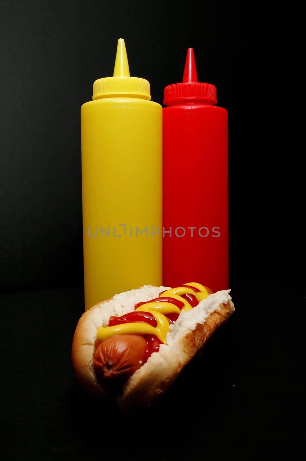 Hot dog with ketchup and mustard bottles.  Isolated on black background.