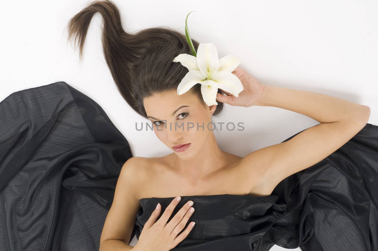 sweet young and cute brunette laying down with a white lily and waved hair