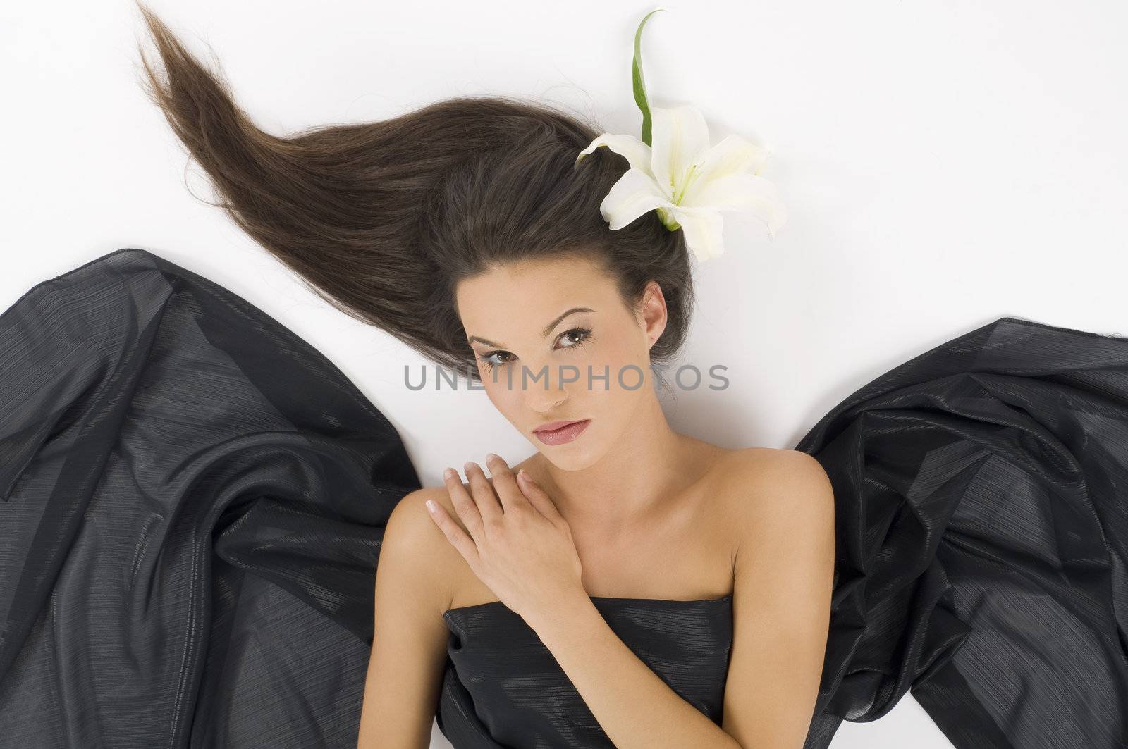 sweet portrait of a young and cute brunette laying down with a white lily in hair