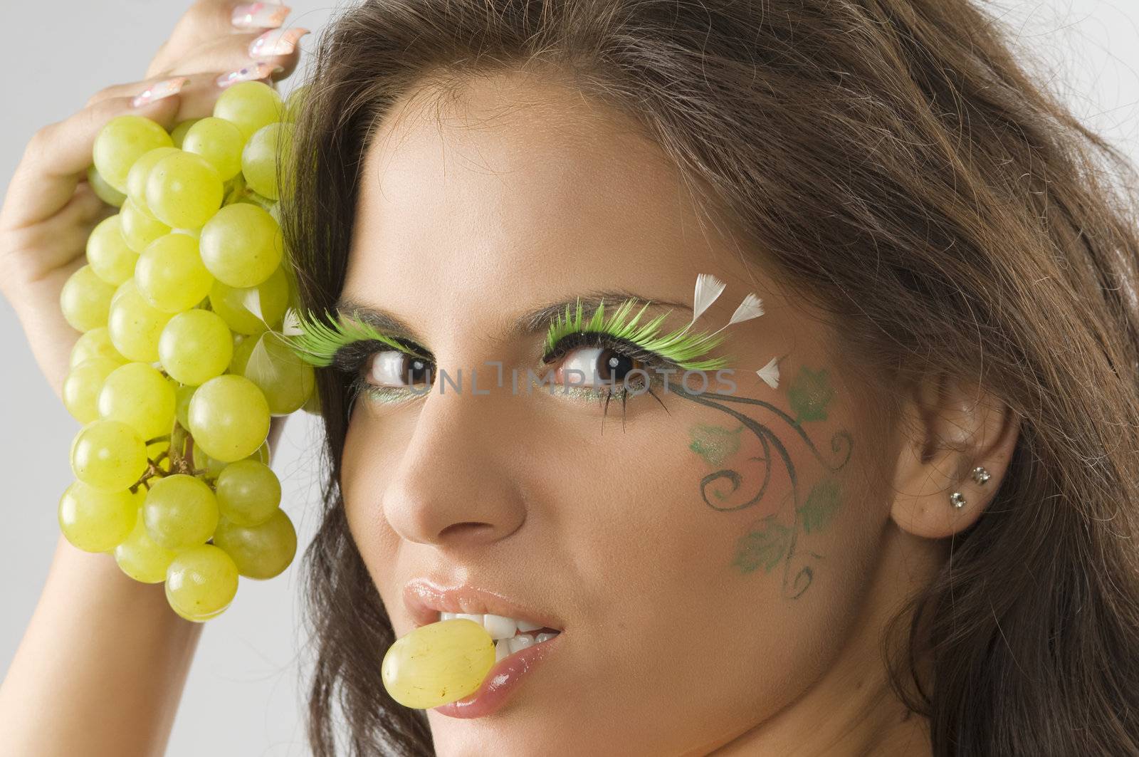 nice girl with a grape between the lips and her face painted with leaf