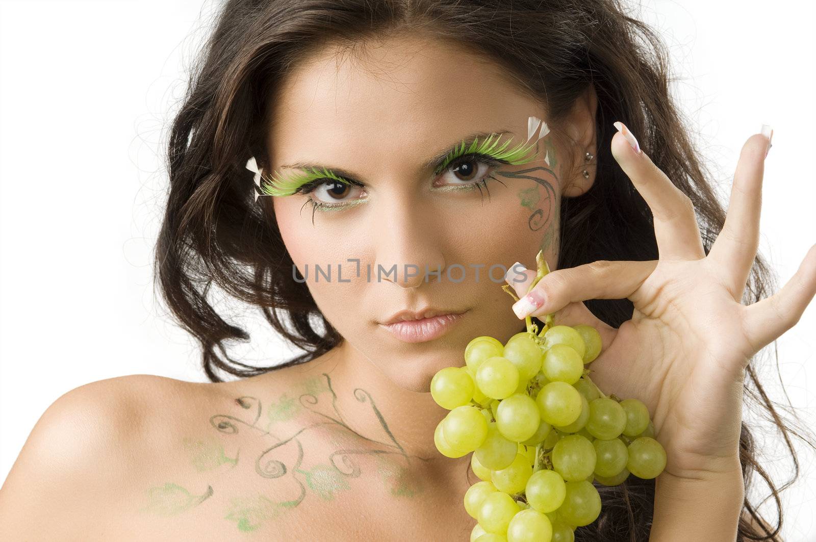 pretty and sensual girl with bodypaint and eyelashes showing grape with hand