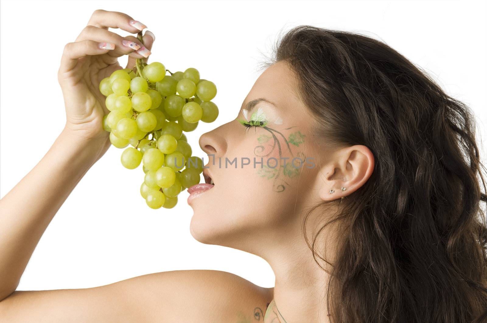 sensual brunette with leaf painted on face licking green grape