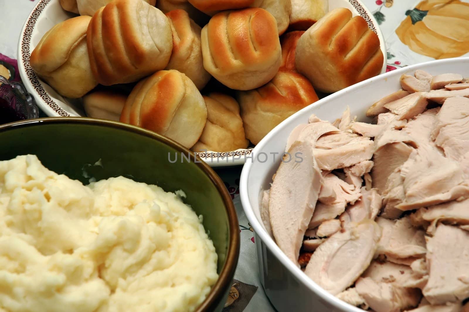 Holiday dinner with sliced turkey, mashed potatoes , and rolls.