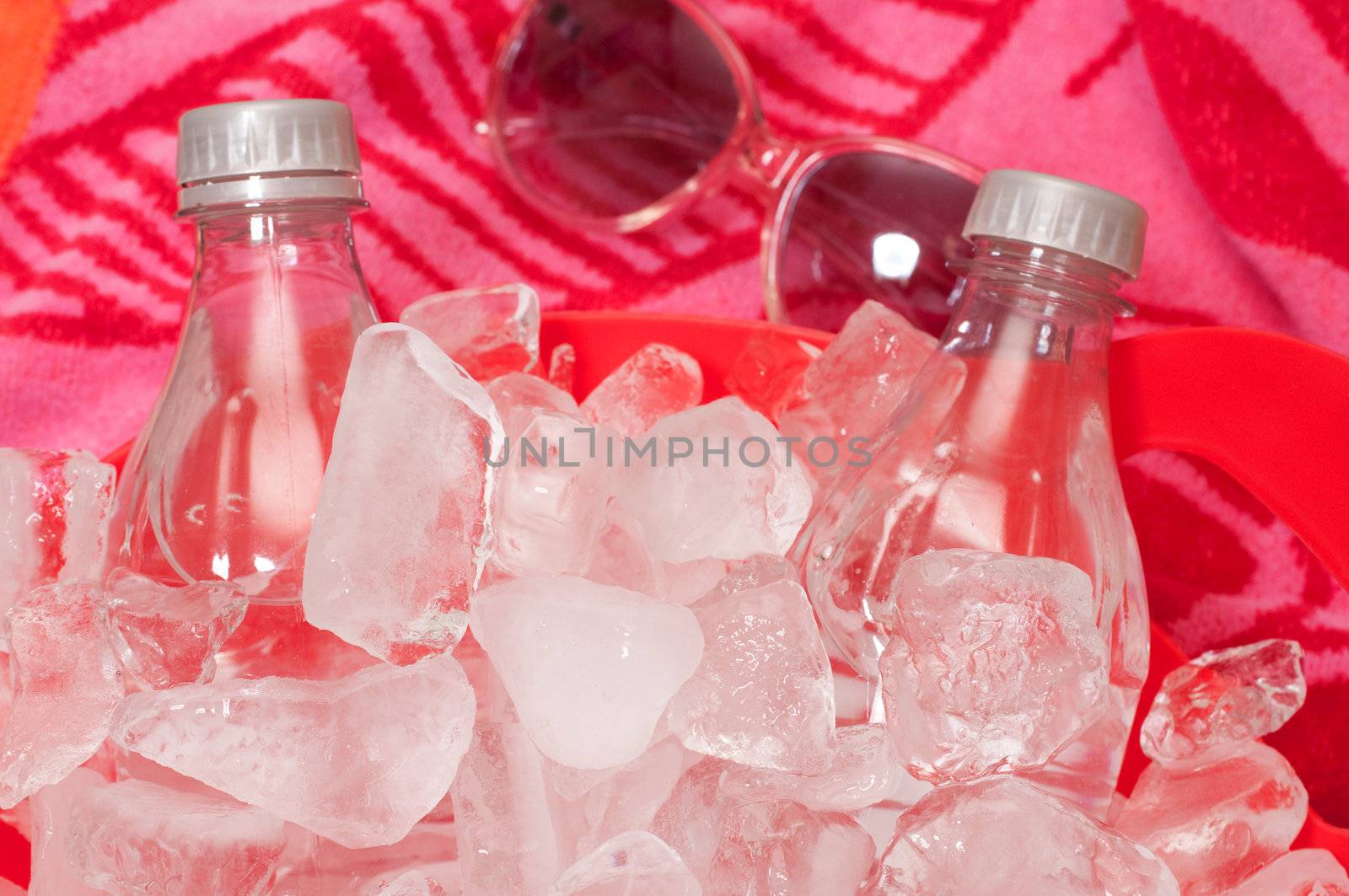 Bottled water in tub of ice with sunglasses and beach towel in background.