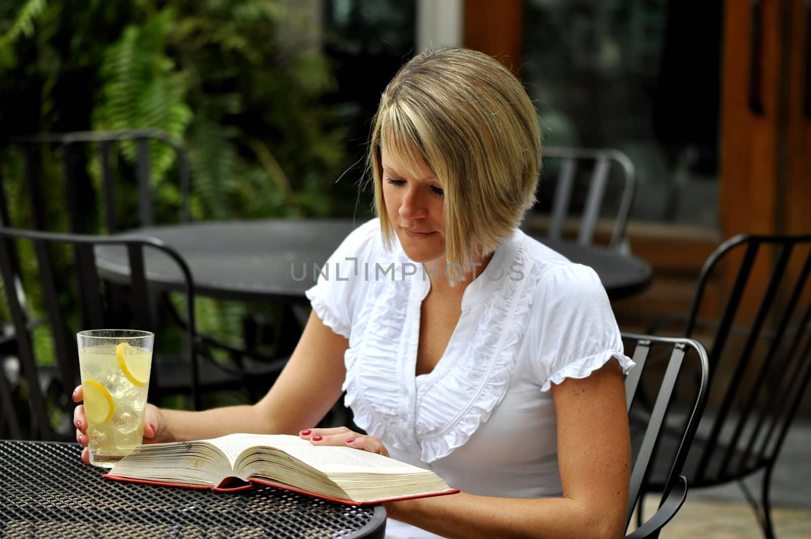 Female blond student reading textbook with glass of lemonade.  