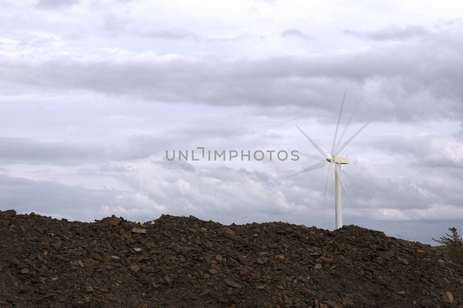 a wind turbine against a calm cloudy sky with rock piles in foreground with blade movement