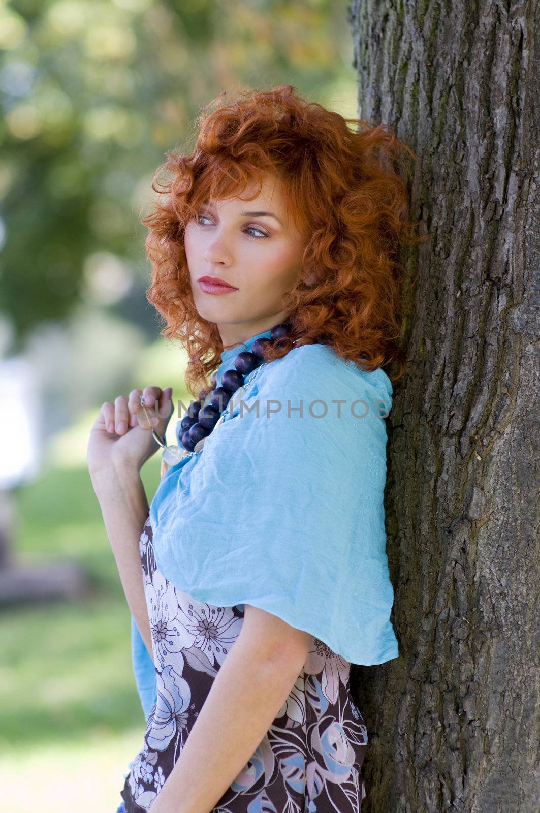 red haired girl in the park standing near the tree with sky-blue scarf